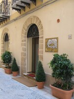 A building with arched doorways, a sign with a crest, and potted plants at the entrance.