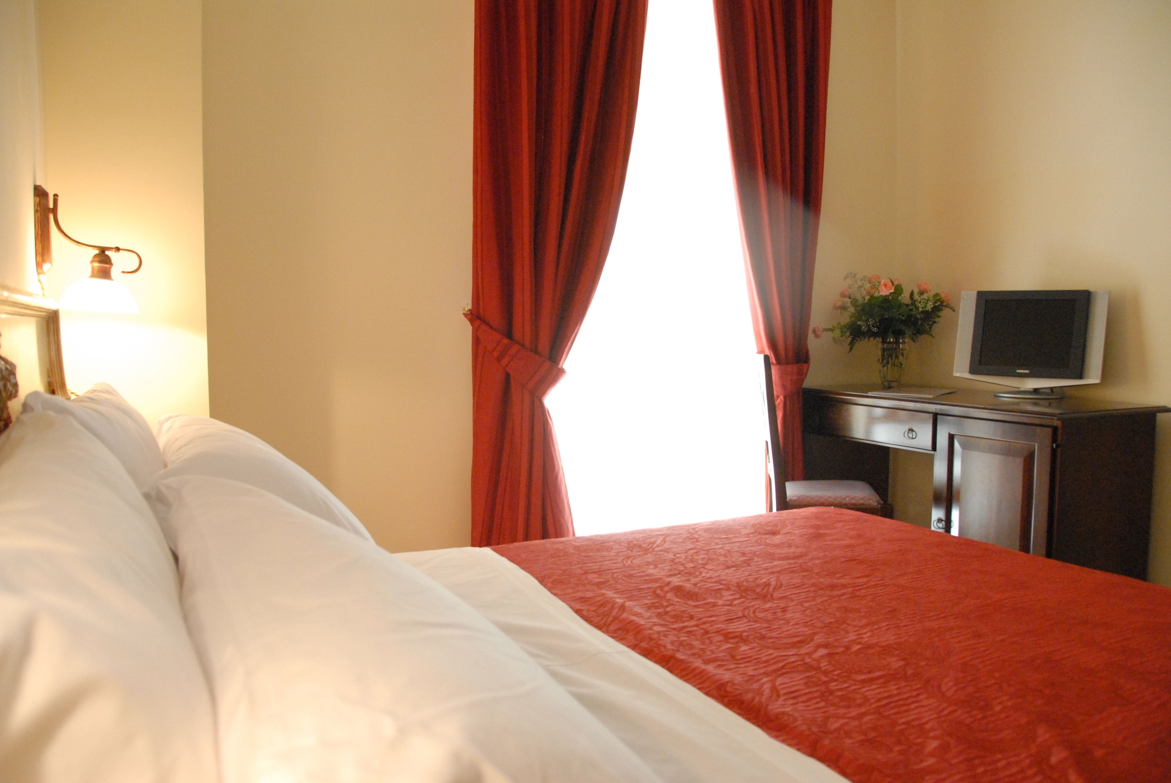 Une chambre d’hôtel avec un lit, un bureau avec une télévision et une fenêtre avec des rideaux.