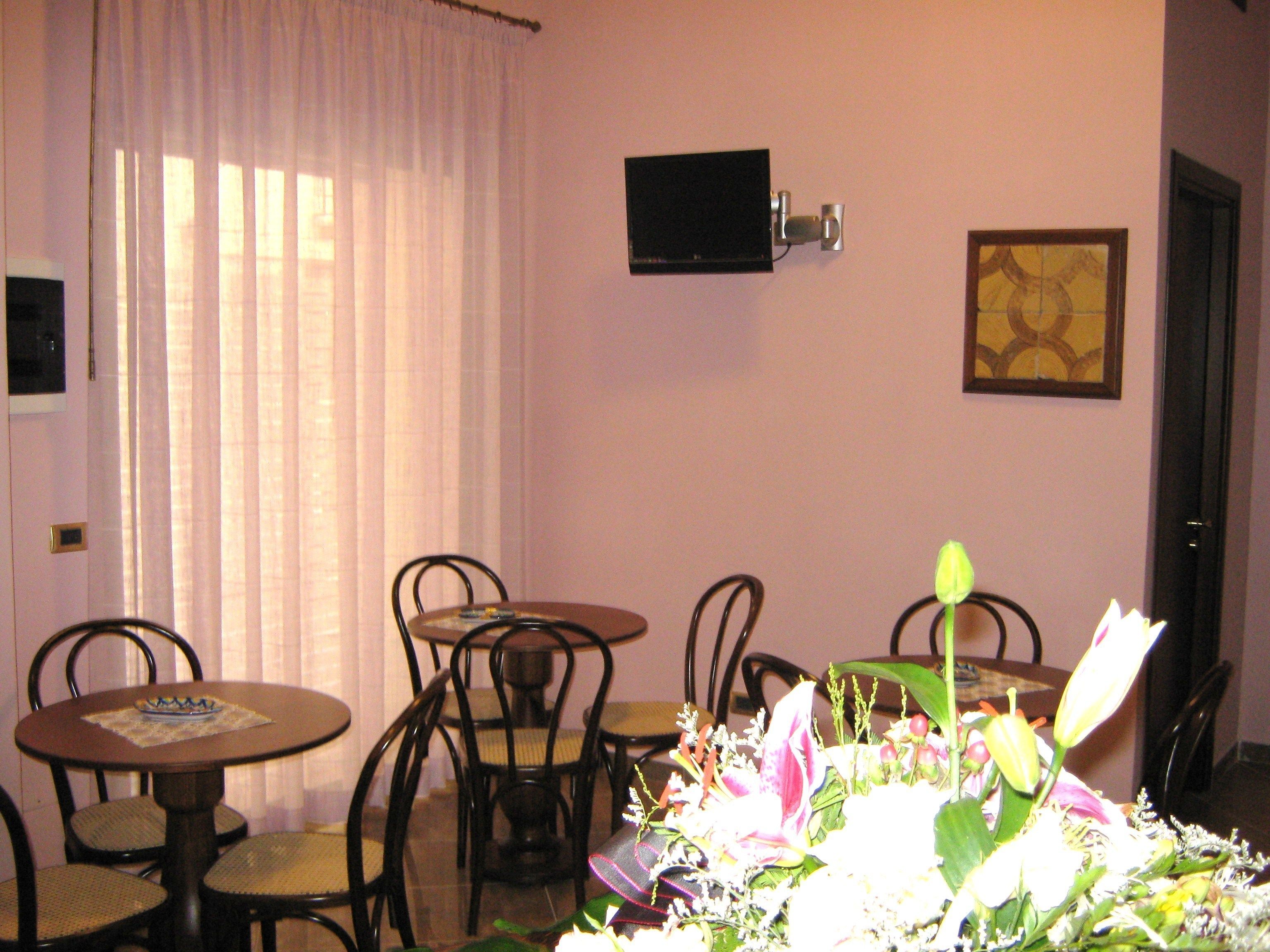 A dining area with a round table, chairs, a flower arrangement, a television mounted on the wall, and a framed picture.