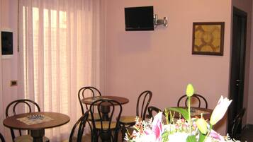 A dining area with a round table, chairs, a flower arrangement, a television mounted on the wall, and a framed picture.
