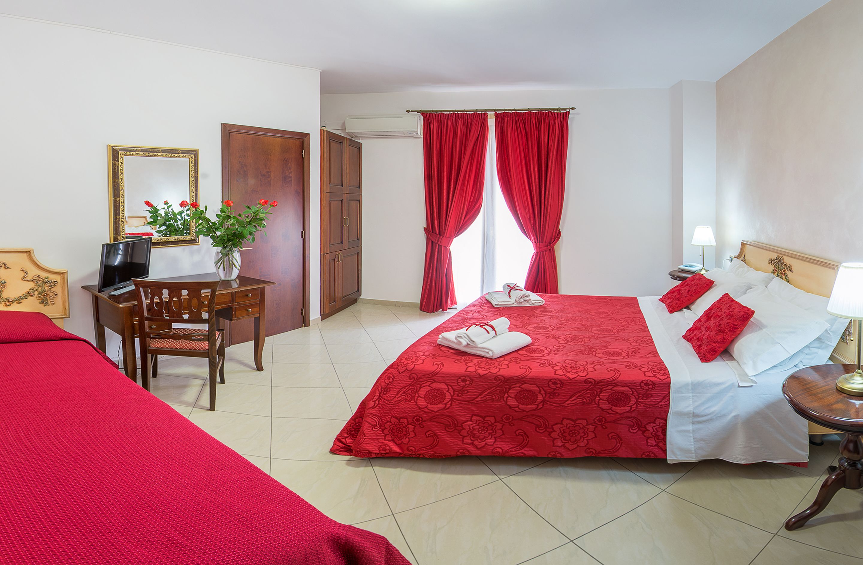 A hotel room with a large bed, a desk with a chair, a TV, and a potted plant.