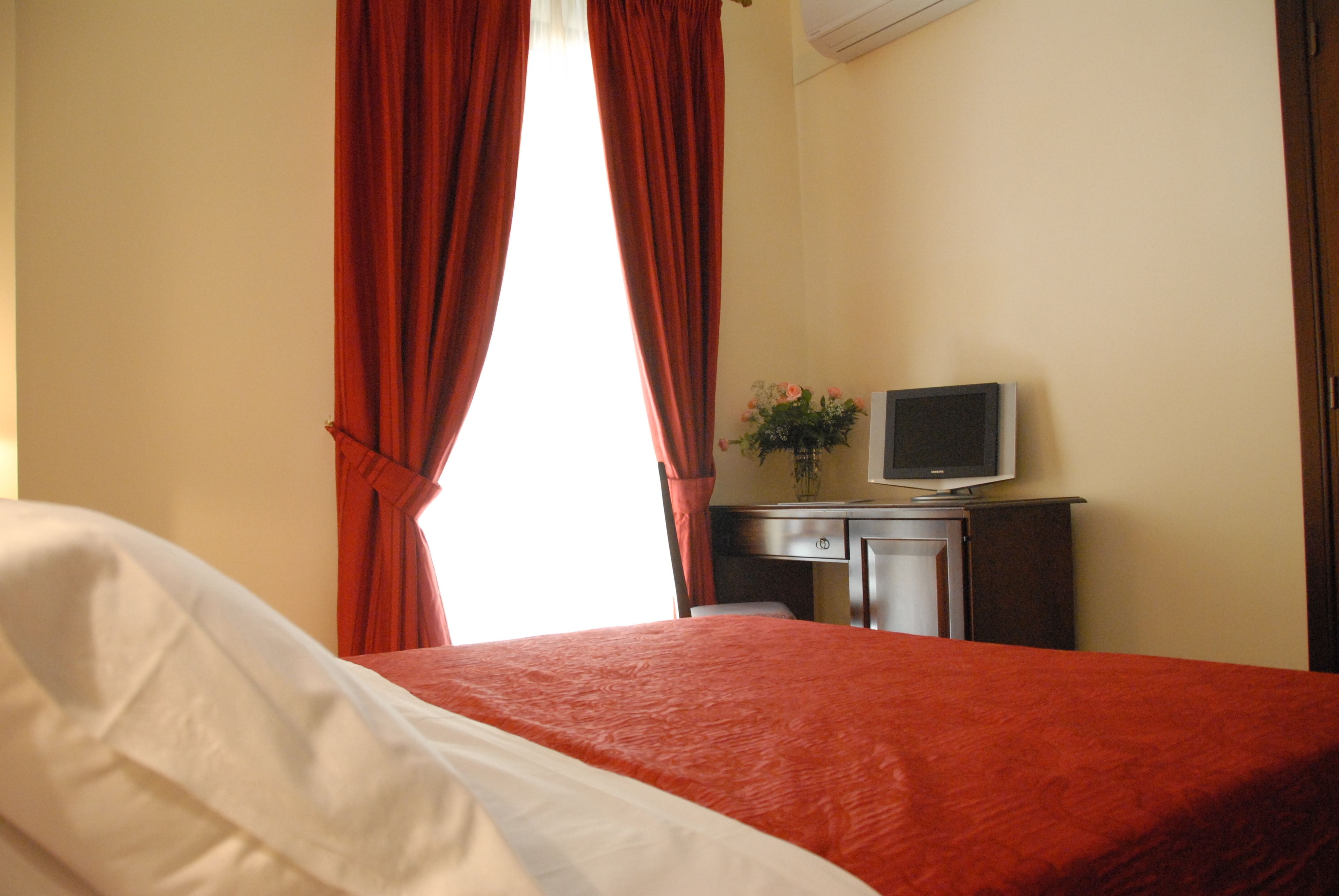 Ein Hotelzimmer mit Bett, Schreibtisch mit Fernseher und Fenster mit roten Vorhängen.