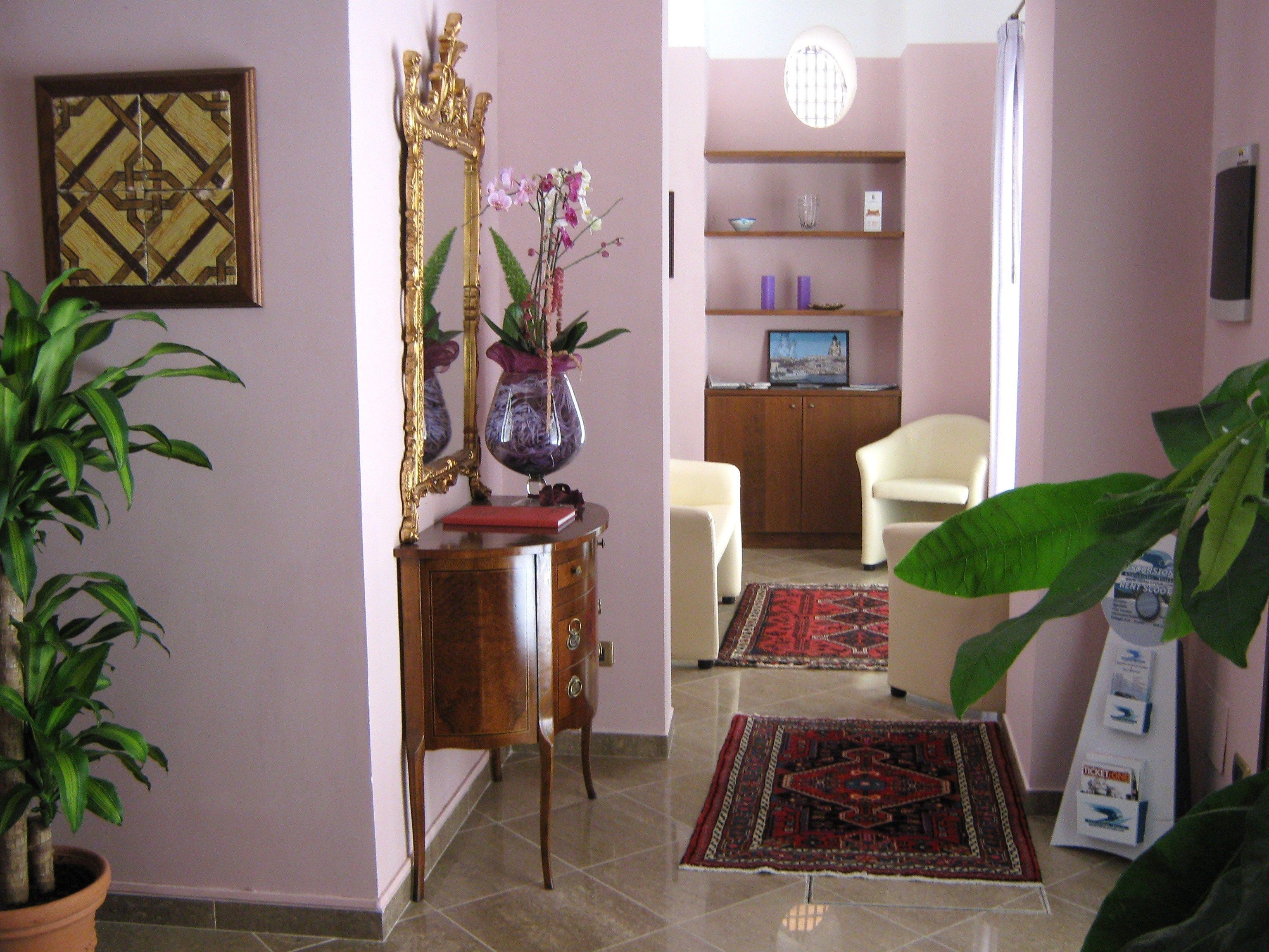 A room with a wooden cabinet, a mirror, a vase with flowers, a television on a shelf, a chair, and a large green plant.