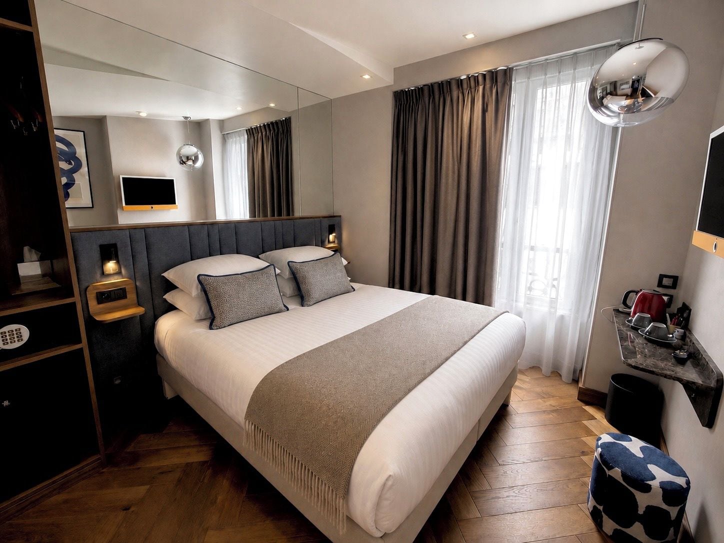 Una habitación de hotel moderna con una cama grande, mesitas de noche, un espejo y vistas al exterior.