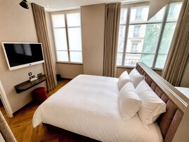 Una camera d'albergo con un letto grande, una TV a schermo piatto fissata al muro e una finestra con tende.