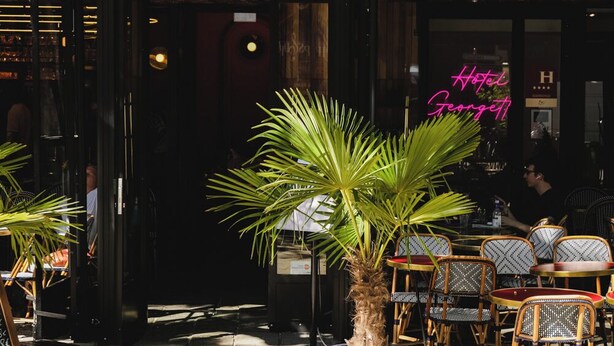A hotel entrance with a blue awning, a neon sign, and outdoor seating with chairs and a palm tree. - Hôtel Georgette (Paris)