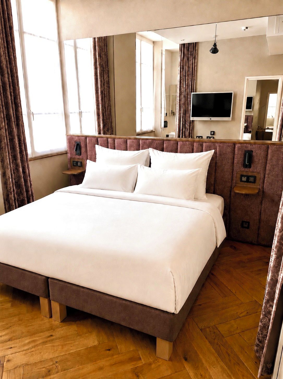 Una habitación de hotel con una cama grande, un televisor de pantalla plana, un espejo y suelo de madera.