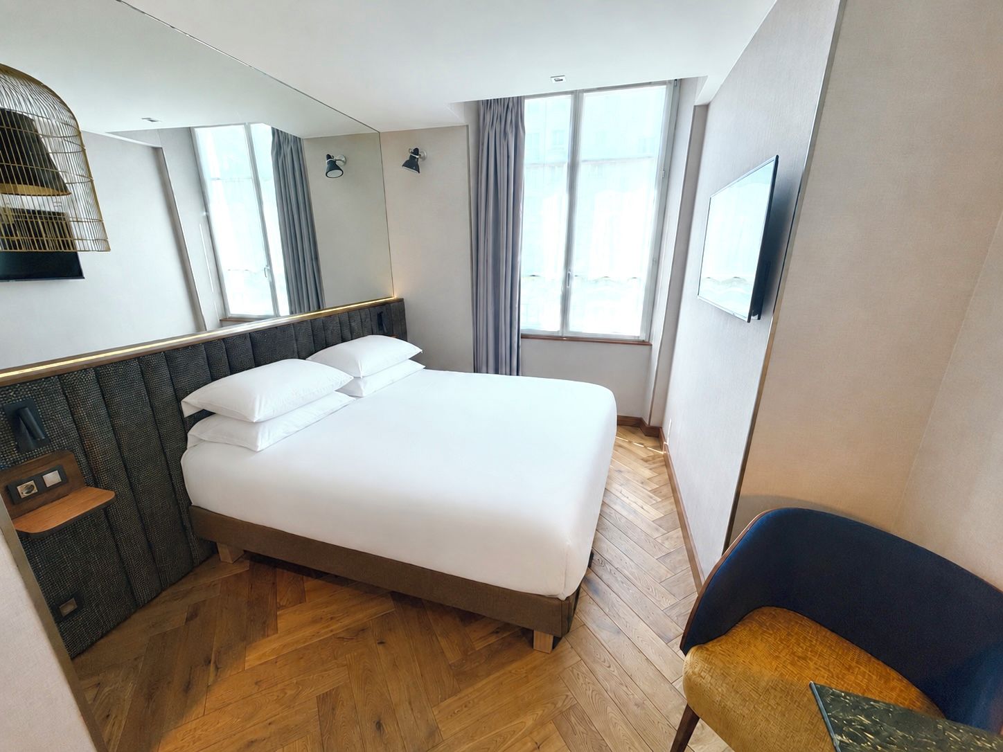 A hotel room with a bed, a chair, a TV, a window, and a mirror.