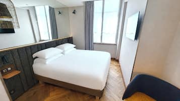 A hotel room with a bed, a chair, a TV, a window, and a mirror.