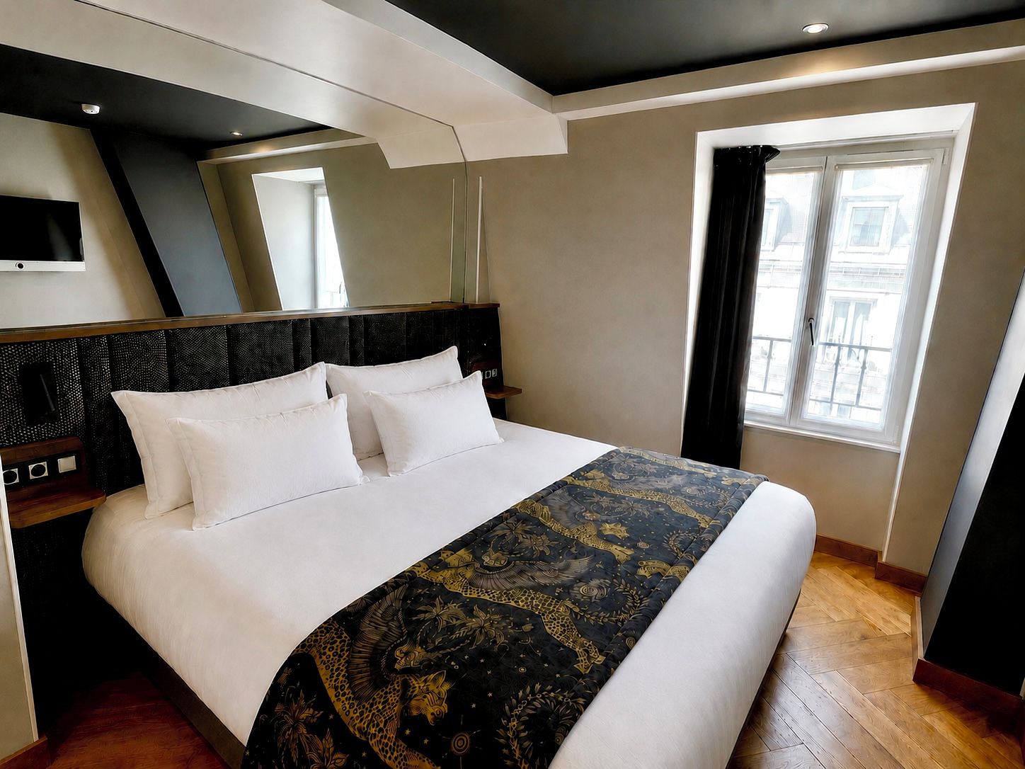 A modern hotel room with a large bed, a flat-screen TV mounted on the wall, and a window with curtains.
