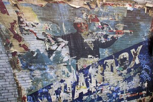 A wall with peeling paint and graffiti, featuring a central figure holding a weapon.