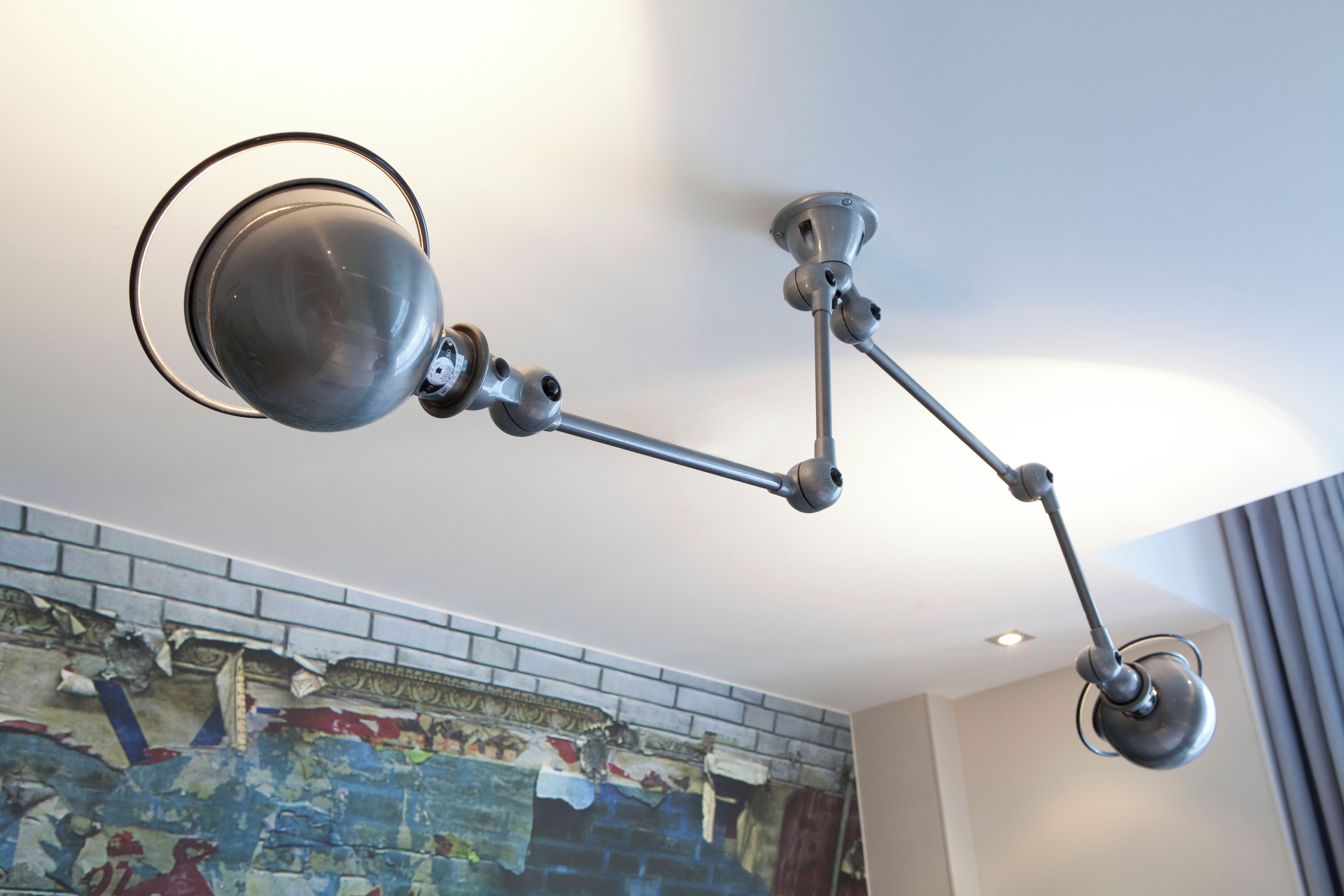 A modern ceiling-mounted lamp fixture with a spherical light and a flexible arm.