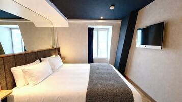 Habitación de hotel con una cama, un televisor de pantalla plana montado en la pared, una ventana con cortinas y una lámpara de techo.