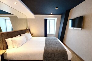 Una camera d'albergo con un letto, una TV a schermo piatto montata a parete, una finestra con tende e una luce a soffitto.