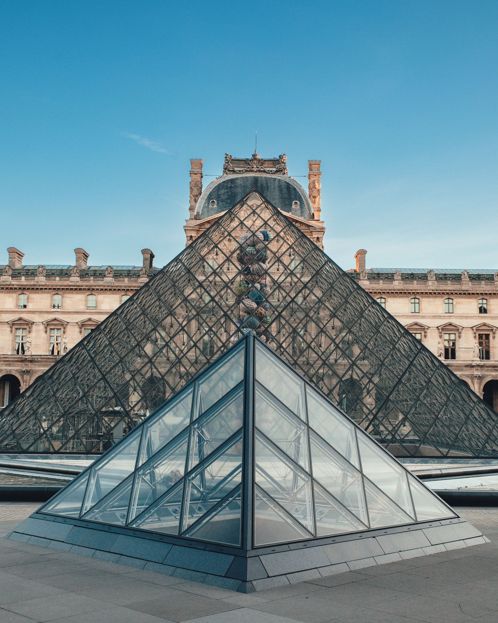 A modern glass pyramid structure in front of the Louvre Museum's iconic glass pyramid.