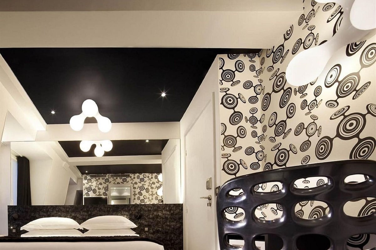 A modern hotel room with a bed, a bathroom, and a unique ceiling design.