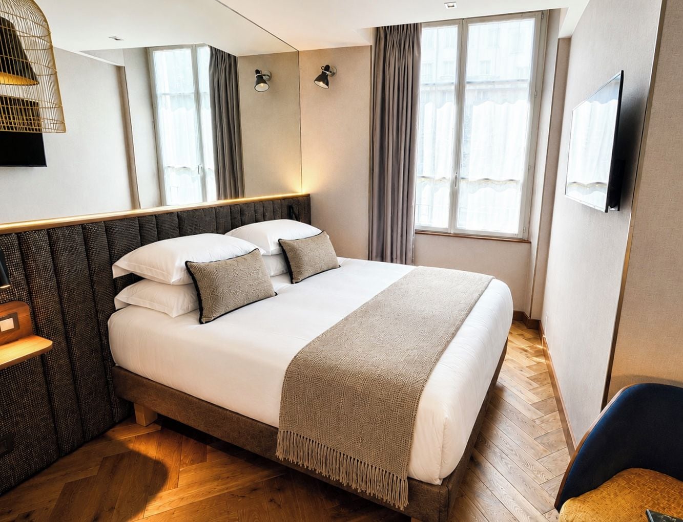 Una habitación de hotel moderna con una cama grande, lámparas de noche, un televisor de pantalla plana y piso de madera.