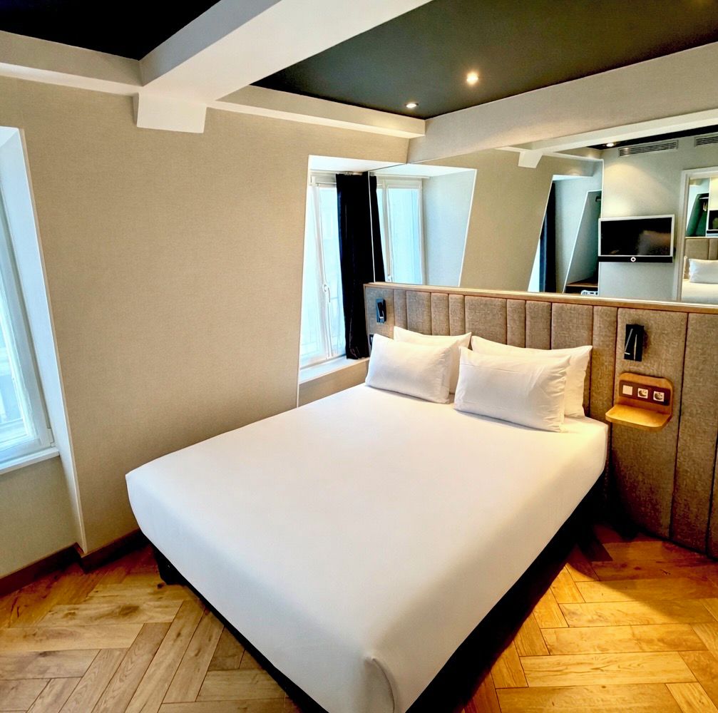 Habitación de hotel con una cama grande, cabecera con controles integrados, televisor y ventana con cortinas.