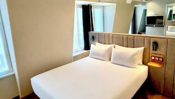 Habitación de hotel con una cama grande, cabecera con controles integrados, televisor y ventana con cortinas.