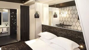A modern bedroom with a large bed, a vanity with a mirror, and a chandelier. - Hôtel Georgette (Paris)