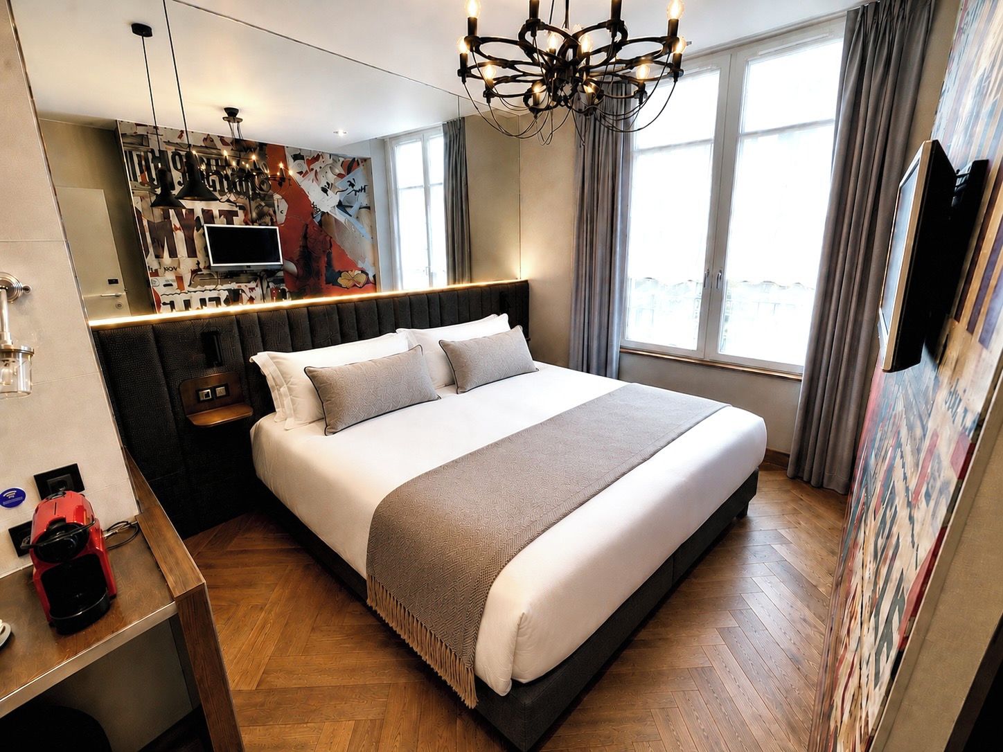 A modern hotel room with a large bed, a television, a coffee maker, and a view of the city through the window.
