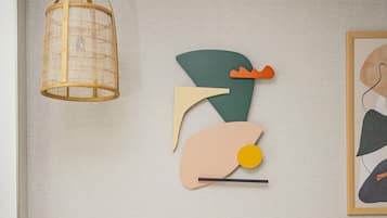 Una cama con almohadas blancas y amarillas, un cabecero con interruptor de luz y arte abstracto en la pared.