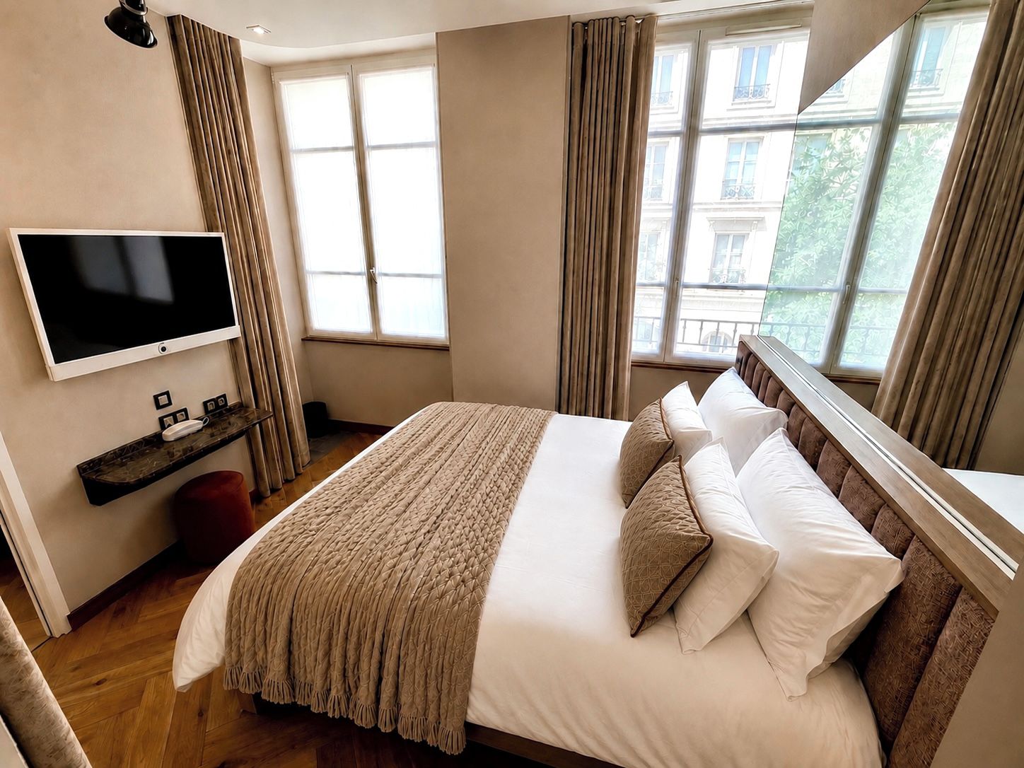 A hotel room with a large bed, a television on the wall, and a window with curtains.