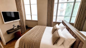A hotel room with a large bed, a television on the wall, and a window with curtains.