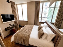 A hotel room with a large bed, a television on the wall, and a window with curtains.