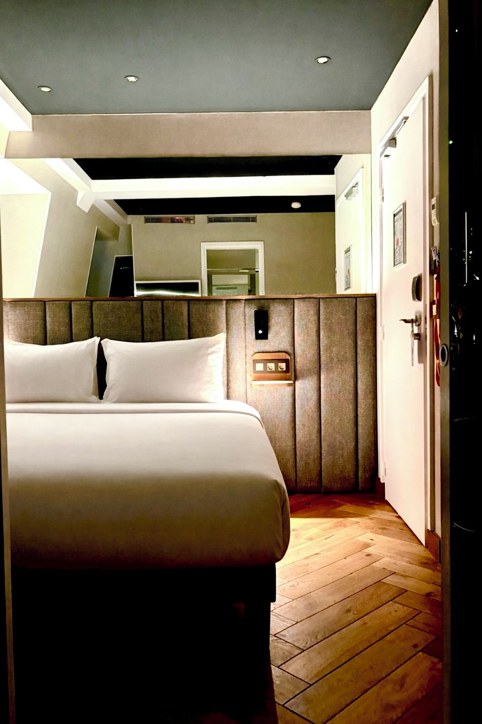 Una habitación de hotel con cama, piso de madera, diseño moderno en el techo y una puerta.