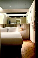A hotel room with a bed, a wooden floor, a modern ceiling design, and a door.
