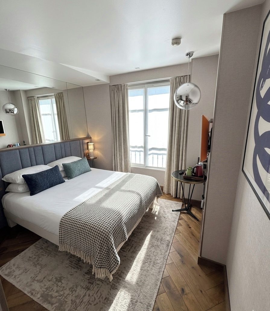 Una habitación de hotel moderna con una cama grande, una mesita pequeña, una silla y un ventanal amplio.