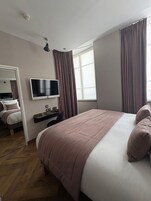 A hotel room with a bed, a desk, a television, and a window with curtains.