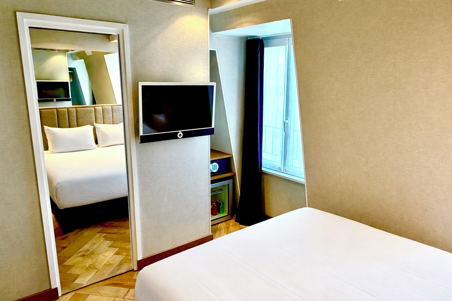 A hotel room with a bed, a TV, a wardrobe, and a window.
