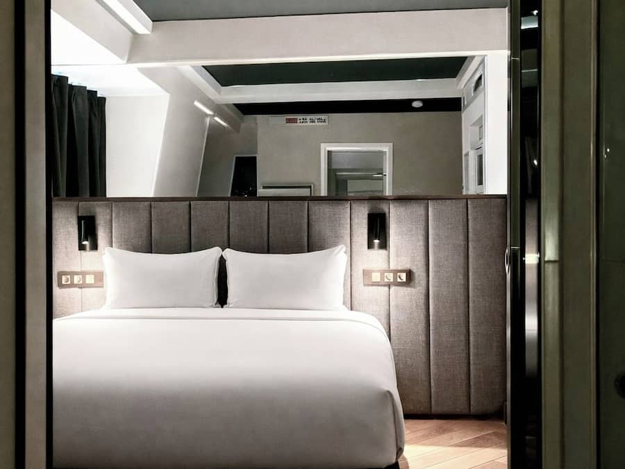 Una habitación de hotel moderna con una cama grande, un cabecero con iluminación integrada y un espejo sobre la cama.