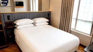 Een hotelkamer met een groot bed, een flatscreen televisie, een nachtkastje, een spiegel en een raam met gordijnen.