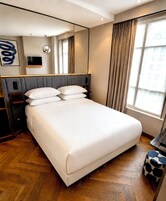 Una camera d'albergo con un letto grande, una TV a schermo piatto, un comodino, uno specchio e una finestra con tende.