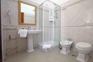 Un baño con ducha envuelta en vidrio, lavamanos pedestal, un bidé y un inodoro.