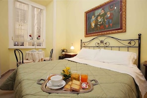 Una cama bien hecha con una bandeja de desayuno, un cuadro en la pared y una ventana con cortinas de encaje.