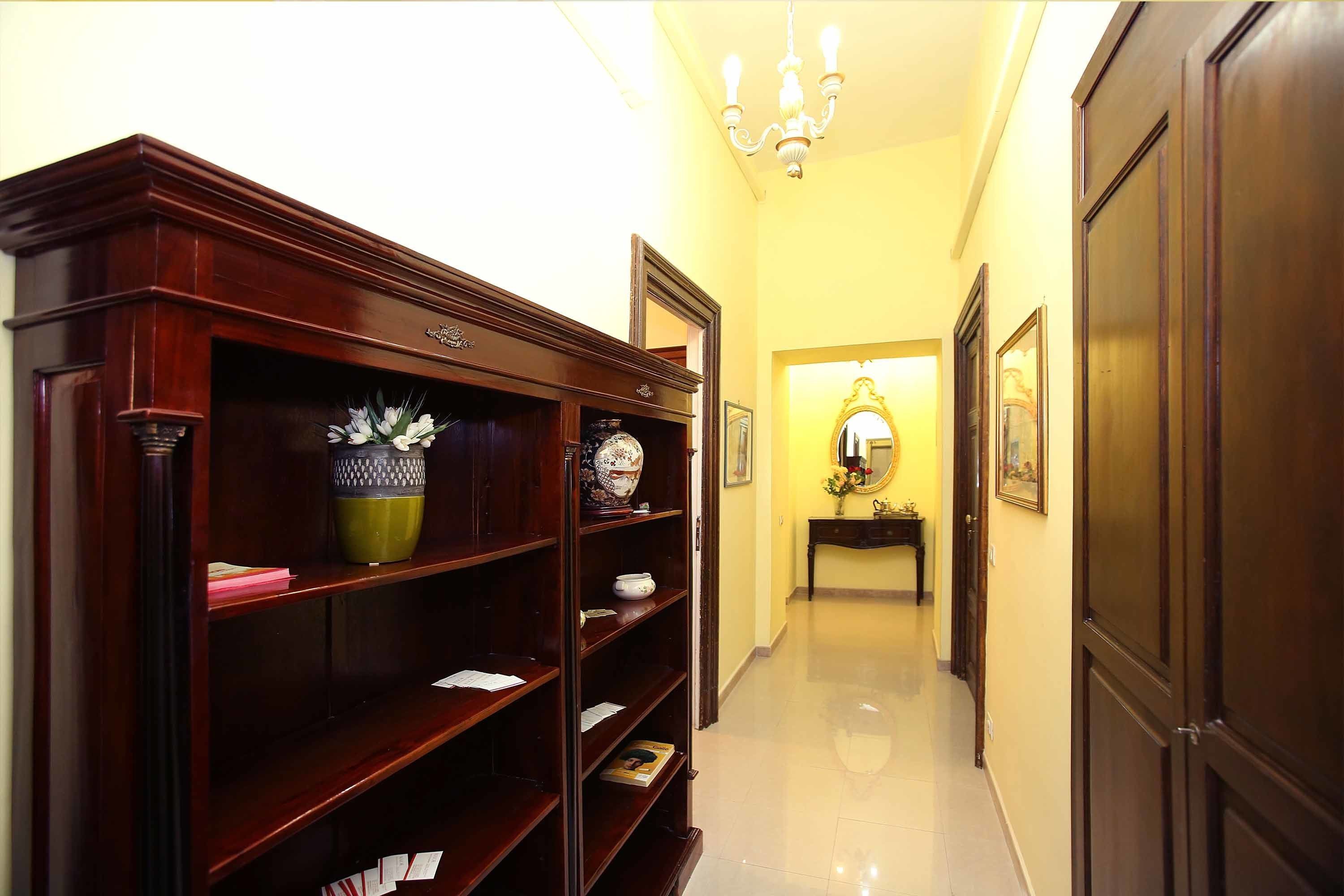 A hallway with a wooden bookcase, a mirror, and a console table with a vase.