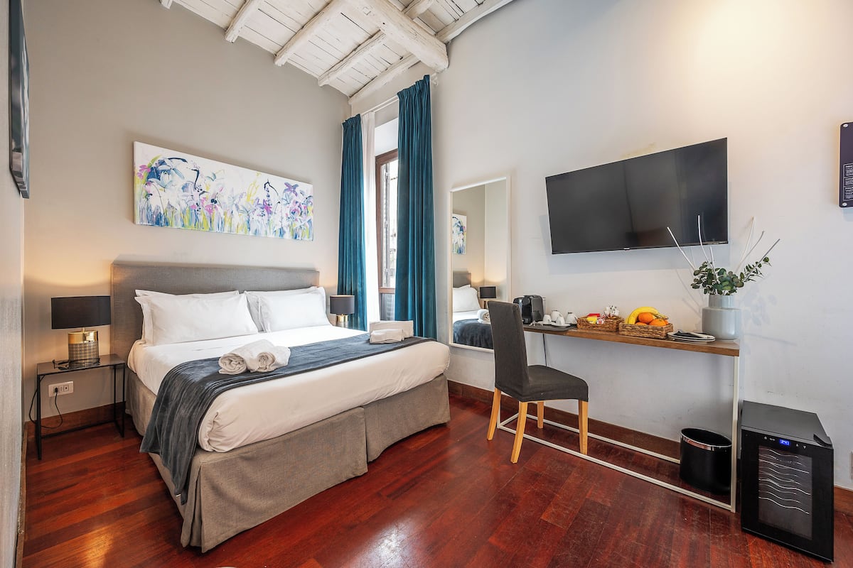 Une chambre d’hôtel comprenant un lit, une table de chevet, une chaise, un bureau, une télévision, des œuvres d’art et une petite kitchenette.