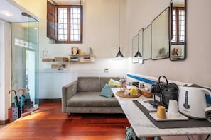 Een moderne woonkamer met een bank, salontafel en een keukenhoek met waterkoker en broodrooster.