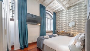 Une chambre d’hôtel avec un lit, une télévision, une fenêtre avec des rideaux, un plancher en bois et un mur orné d’un motif.