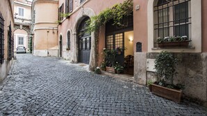 A cobblestone street with a building featuring arched windows and a door, potted plants, and a car parked in the background. - Arco del Lauro Bed & Breakfast (Rome)