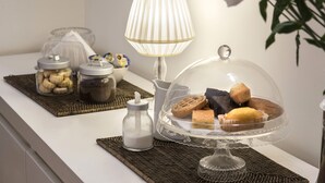 A table with a clear glass dome displaying pastries, a lamp, and jars of nuts and chocolates. - Arco del Lauro Bed & Breakfast (Rome)