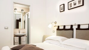 A bedroom with a bed, pillows, a nightstand, a wall-mounted lamp, a mirror, and a framed picture. - Arco del Lauro Bed & Breakfast (Rome)