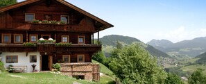 Eine Holzhütte mit Balkon, Steinstufen und Blick auf die umliegenden Hügel.
