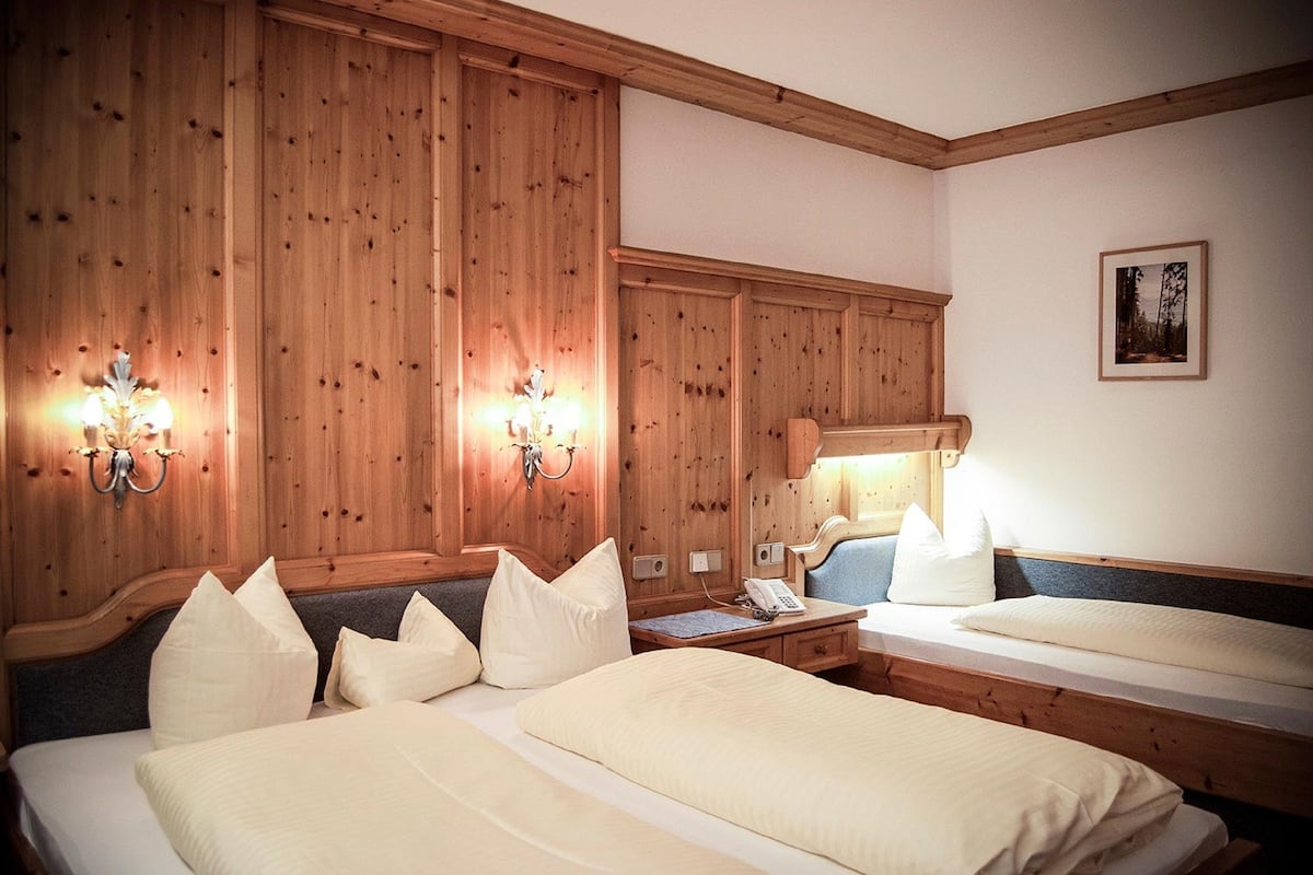 A hotel room with wooden panel walls, two beds with white bedding, a bedside table with a lamp, and a framed picture on the wall.