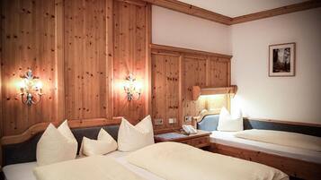 Une chambre d’hôtel avec des murs lambrissés, deux lits avec du linge de lit blanc, une table de chevet avec une lampe et un tableau encadré au mur.