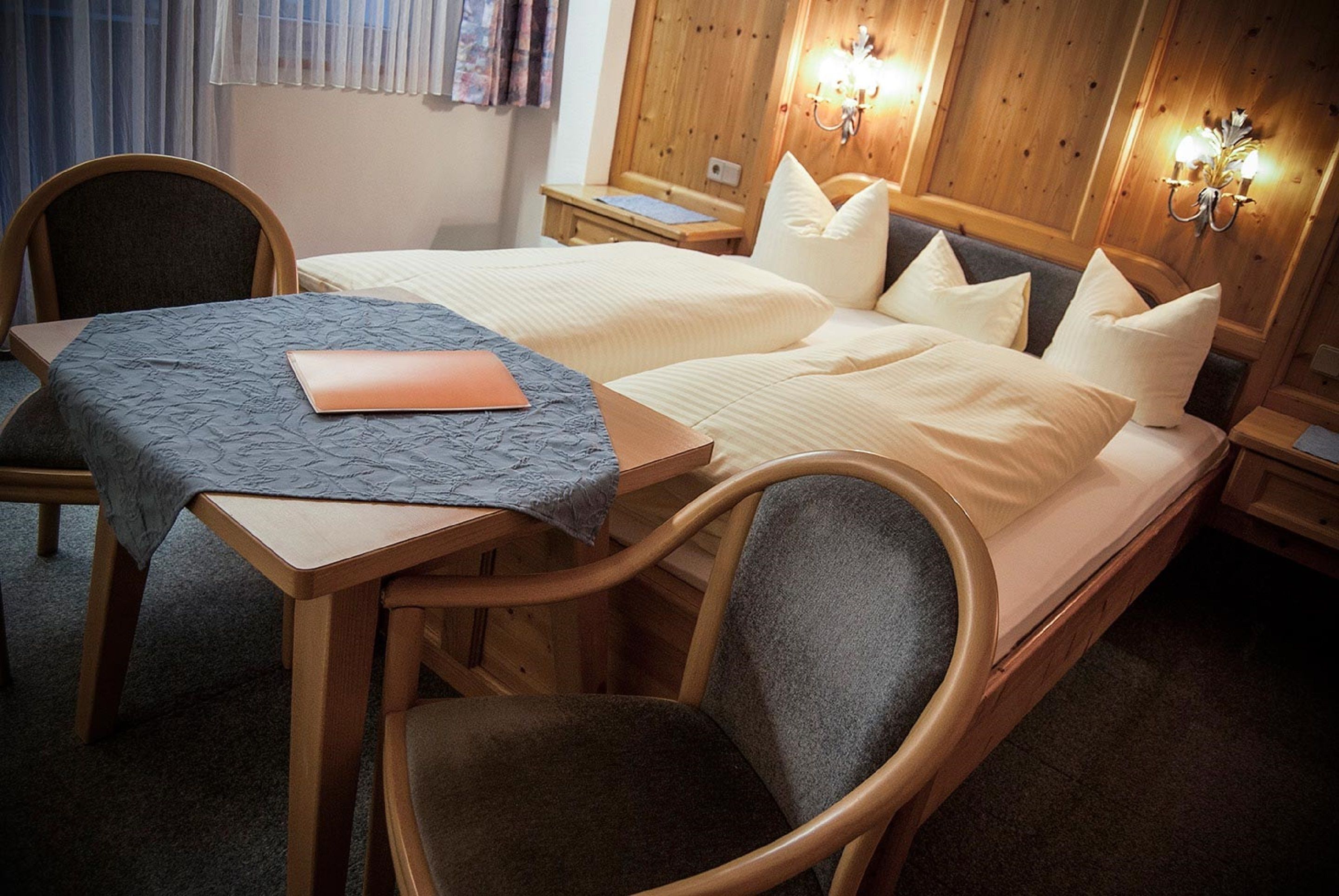 A hotel room with two beds, a wooden desk, a chair, and a nightstand.
